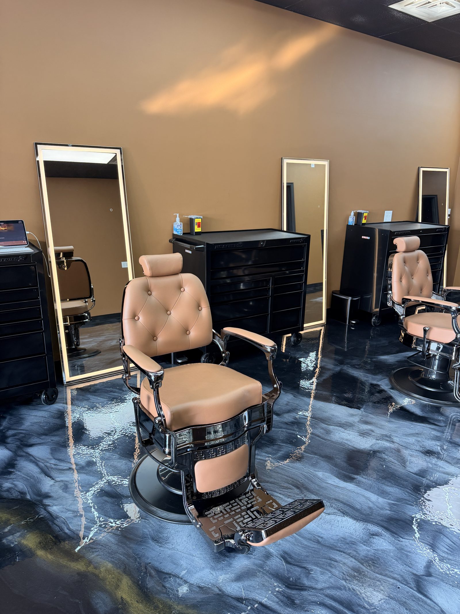 Inside Exclusive Barber Studio — tan leather chairs, chrome bases, gold-framed mirrors, and black epoxy floors.